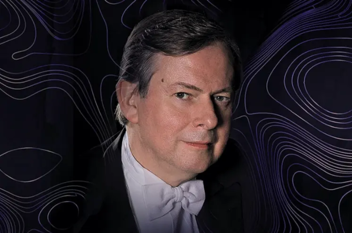 Krzysztof Jabłoński wearing a tuxedo and white bow tie, against a dark background decorated with purple, wavy lines.