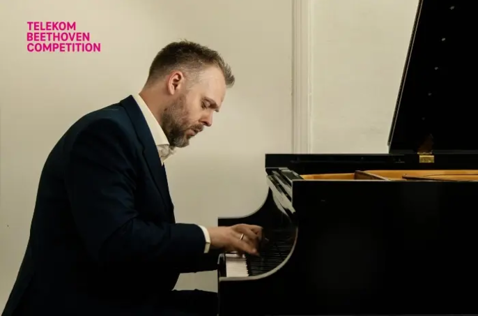 Pianista Hinrich Alpers gra na fortepianie, ukazany z profilu w jasnym wnętrzu.
